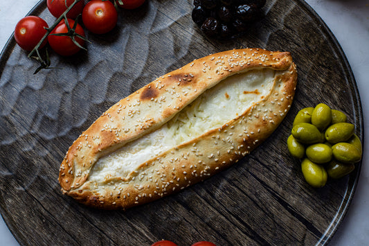 Baked dish with sesame seeds on a wooden board with olives and tomatoes.