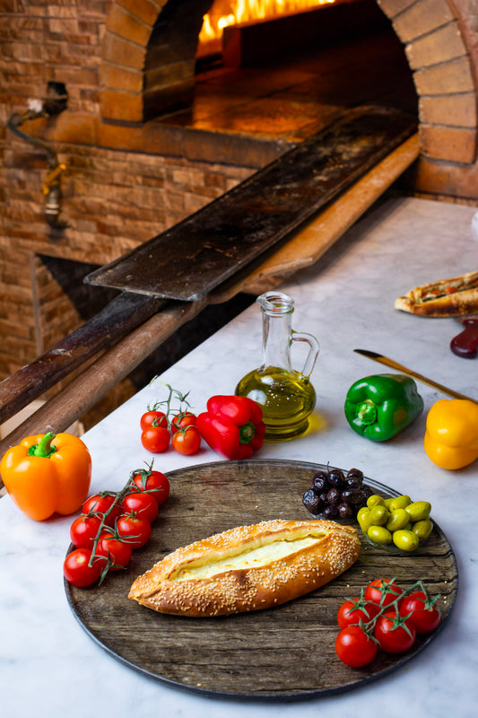 Wooden board with bread and vegetables in front of a brick oven